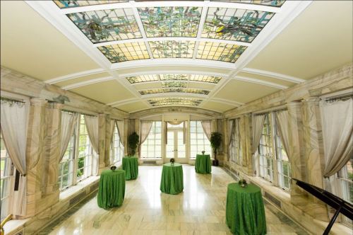 A bright room with stained glass ceilings, featuring green tablecloths on round tables and large windows.