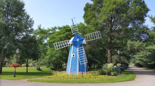 A blue windmill surrounded by trees and flowers, set along a peaceful pathway.
