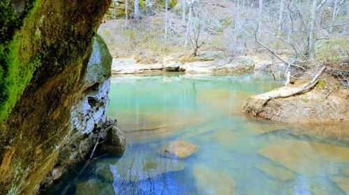 A serene river scene with clear water, rocky banks, and trees in a peaceful, natural setting.