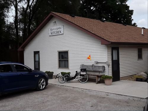 A small white building with a brown roof, labeled "Bar & Grill Kitchen," parked car, and a bicycle outside.