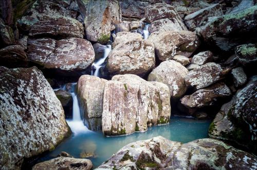 A serene waterfall cascading over large, moss-covered rocks into a tranquil blue pool.