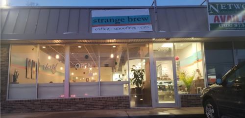 Exterior of "Strange Brew" café with a sign, large windows, and a welcoming atmosphere at dusk.