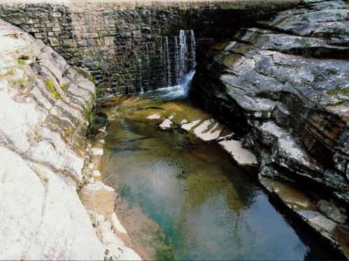 A serene rocky landscape featuring a small waterfall cascading into a clear pool surrounded by stone formations.