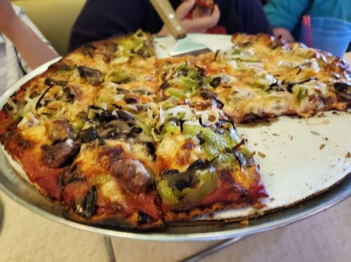 A close-up of a pizza topped with green peppers, olives, and melted cheese, served on a round metal tray.