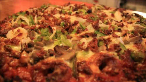 Close-up of a pizza topped with green peppers, mushrooms, onions, and crispy bacon on a golden crust.