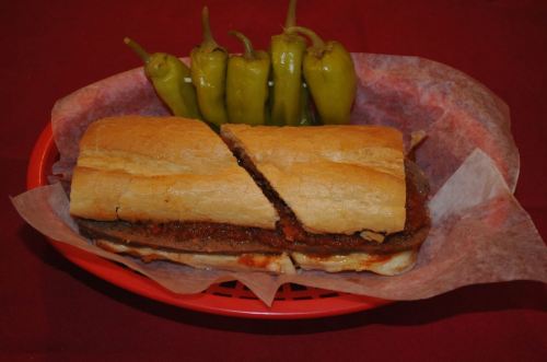 A sandwich with meat and sauce, cut in half, served in a red basket with green peppers on the side.