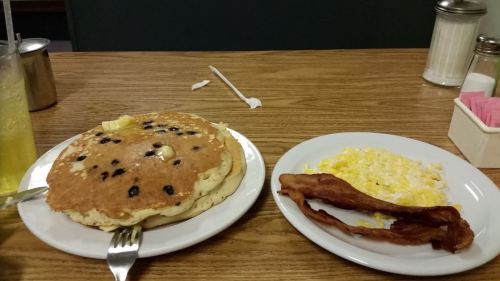 A plate with large blueberry pancakes, scrambled eggs, and crispy bacon on a wooden table.