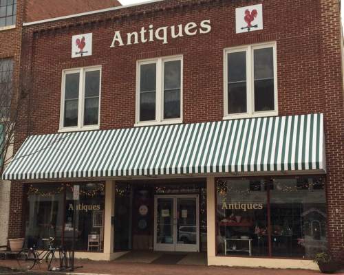 A brick building with a green and white striped awning, featuring "Antiques" signage and a bicycle outside.