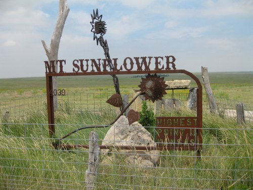Sign for Mt. Sunflower, the highest point in Kansas, featuring a metal sunflower design and surrounded by grasslands.