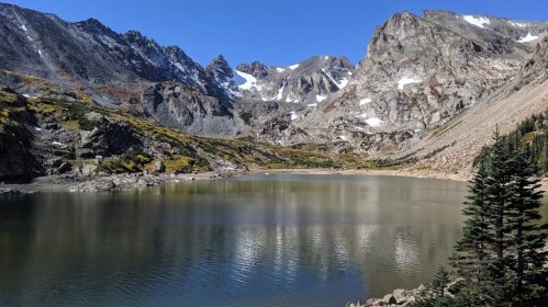 A serene mountain lake surrounded by rugged peaks and colorful autumn foliage under a clear blue sky.