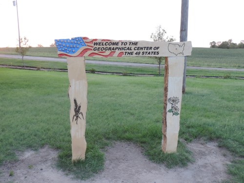 Welcome sign for the Geographical Center of the 48 States, featuring an American flag and local flora engravings.