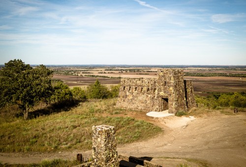 A stone structure on a hilltop with a panoramic view of fields and distant hills under a clear blue sky.