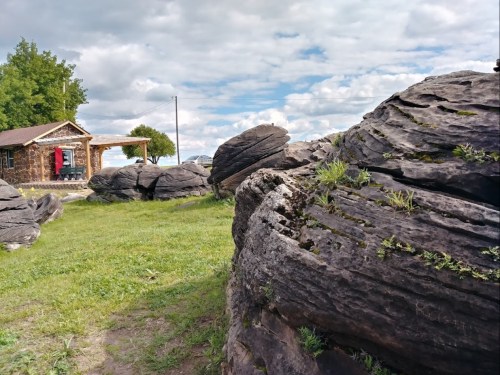 A rocky landscape with large, textured boulders, a wooden cabin, and a cloudy sky in the background.