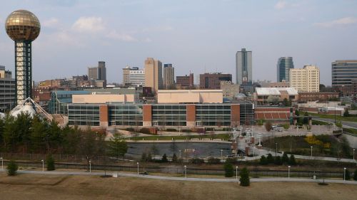 A city skyline featuring modern buildings and a distinctive gold sphere structure, with green spaces in the foreground.