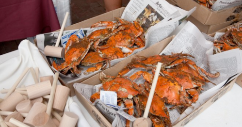 Boxes of cooked crabs on newspaper, with wooden mallets beside them, displayed at a seafood market.