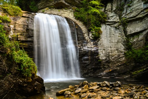 A serene waterfall cascades over rocky cliffs into a calm pool, surrounded by lush greenery.