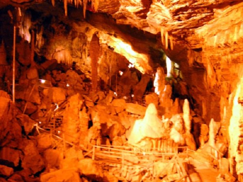 A dimly lit cave with rock formations, stalactites, and a wooden pathway winding through the rocky terrain.