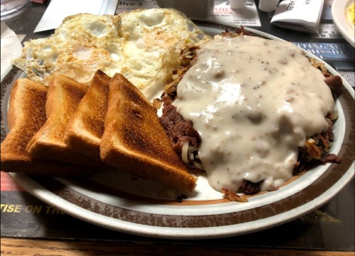 A plate of hash browns topped with sausage gravy, served with two fried eggs and three slices of toast.