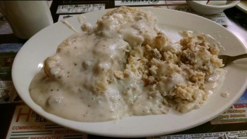 A plate of biscuits smothered in creamy sausage gravy, served with a side of crumbled biscuit.