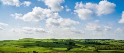 Lush green hills under a bright blue sky with fluffy white clouds. A serene and expansive landscape.