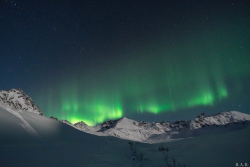 A stunning display of the northern lights illuminates a snowy mountain landscape under a starry night sky.