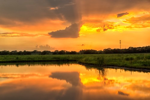 A serene sunset over a calm lake, with vibrant orange and yellow hues reflecting on the water's surface.