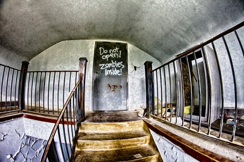 A dimly lit staircase leads to a door with a warning: "Do not open! Zombies inside!" Graffiti decorates the walls.