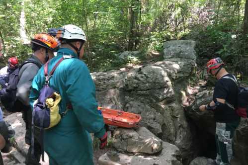 Rescue team in helmets and gear near a rocky area, preparing to assist someone in a cave or crevice.