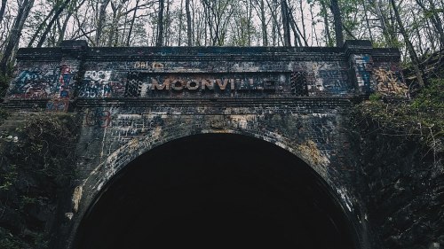 A dark tunnel entrance with "Moonville" sign, surrounded by trees and covered in colorful graffiti.