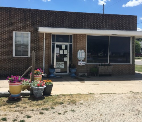 A brick building with large windows, a door, and flower pots in front, set against a clear blue sky.