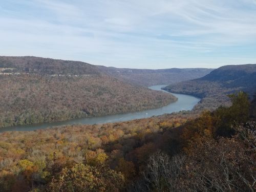 A scenic view of a winding river surrounded by autumn foliage and rolling hills under a clear sky.