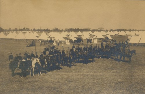 A historical black-and-white photo of soldiers on horseback in front of military tents.