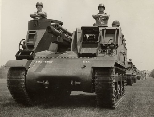 Two soldiers stand atop military tanks lined up on a grassy field, facing forward in a historical black-and-white photo.