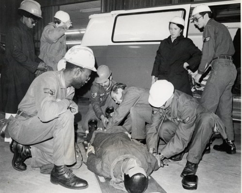 A group of emergency responders in helmets assists an injured person on a stretcher in a training setting.