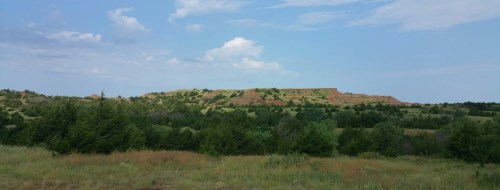A panoramic view of rolling hills and green fields under a blue sky with scattered clouds.