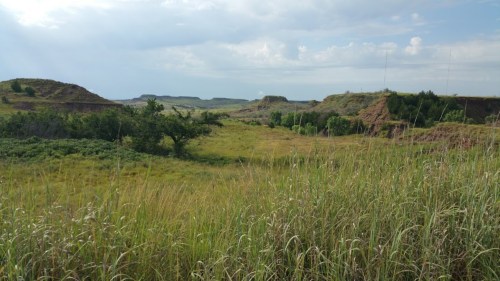 A scenic landscape featuring rolling hills, green vegetation, and a cloudy sky in the background.