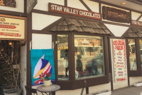 A quaint shopfront featuring "Star Valley Chocolates" with colorful signage and a sailboat flag hanging outside.