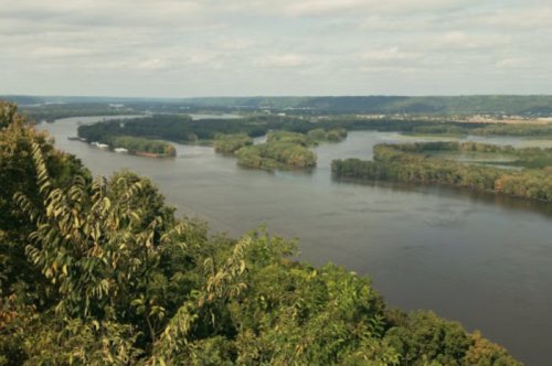 A scenic view of a river winding through lush green islands under a cloudy sky.