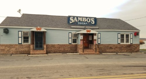 Exterior of Sambo's Tavern, a blue building with a sign, crab decorations, and steps leading to the entrance.