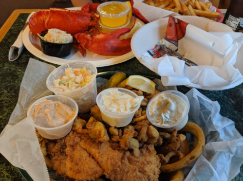 A seafood feast featuring a lobster, fries, coleslaw, and fried fish with dipping sauces on a table.