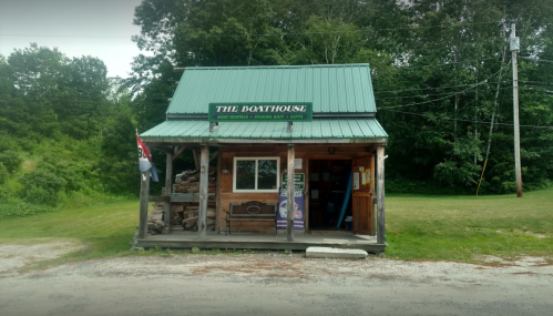 A small wooden building with a green metal roof, labeled "The Boathouse," surrounded by trees and grass.