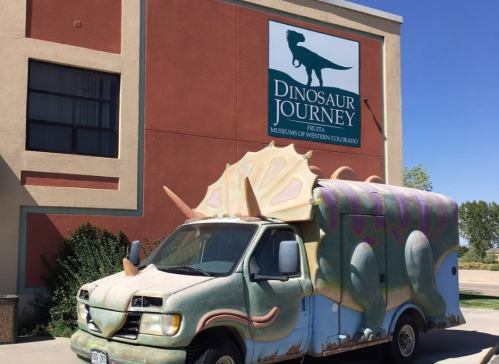 A colorful dinosaur-themed van parked outside the Dinosaur Journey museum in Fruita, Colorado.