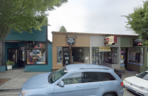 A street view of shops, including a gelato store, with a parked blue SUV in front. Trees line the sidewalk.