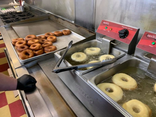A kitchen scene with freshly fried donuts in a fryer and a tray of cooked donuts on the counter.