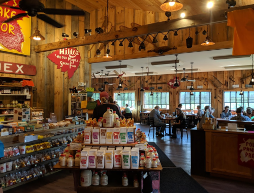 A cozy shop with wooden decor, shelves of products, and customers enjoying meals at tables in the background.