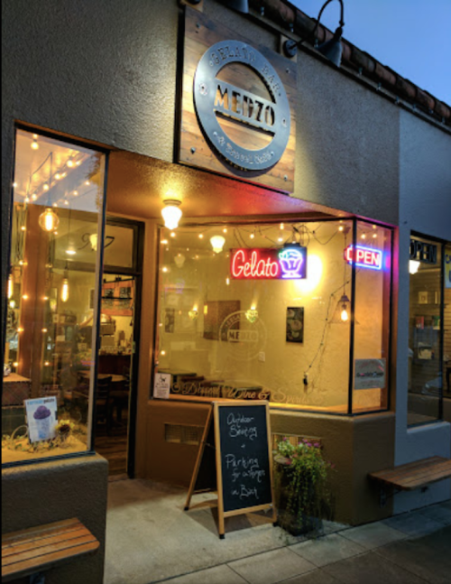 Cozy gelato shop exterior at dusk, featuring warm lights, an "Open" sign, and a chalkboard menu outside.