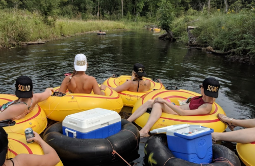 A group of people in inner tubes floating on a river, wearing matching hats and enjoying drinks.