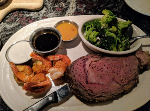 A plate featuring prime rib, grilled shrimp, broccoli, and dipping sauces.
