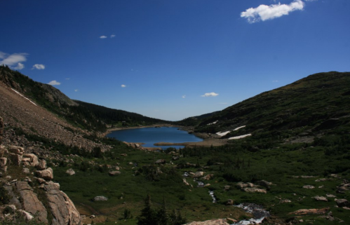 A serene mountain landscape featuring a blue lake surrounded by rocky hills and lush greenery under a clear blue sky.