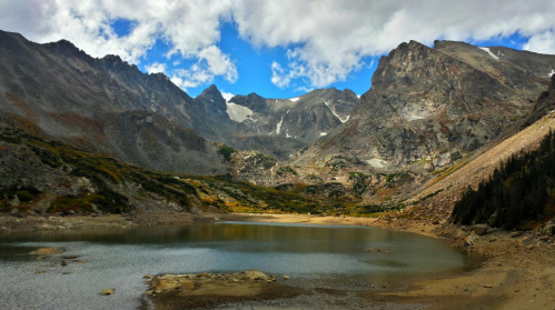 A serene mountain landscape with a calm lake, rocky terrain, and dramatic clouds overhead.